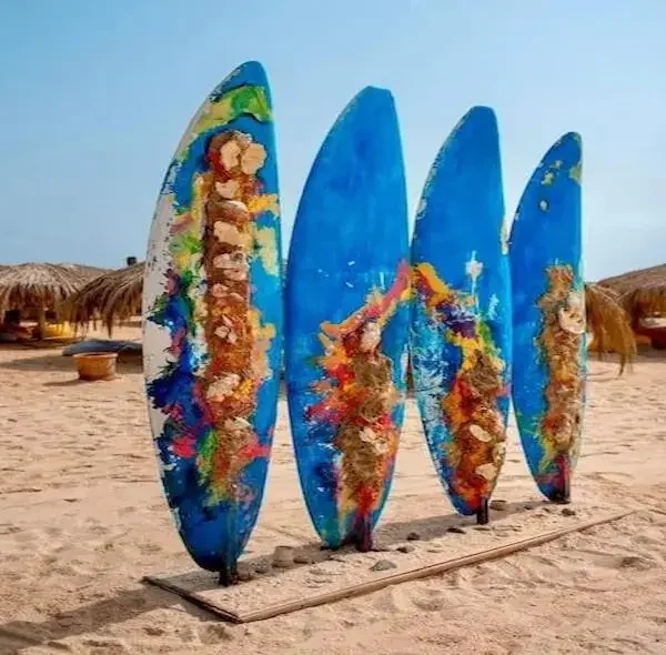 Four brightly painted decorative surfboards standing on the sand at Paradise Island Hurghada with beach umbrellas in the background.
