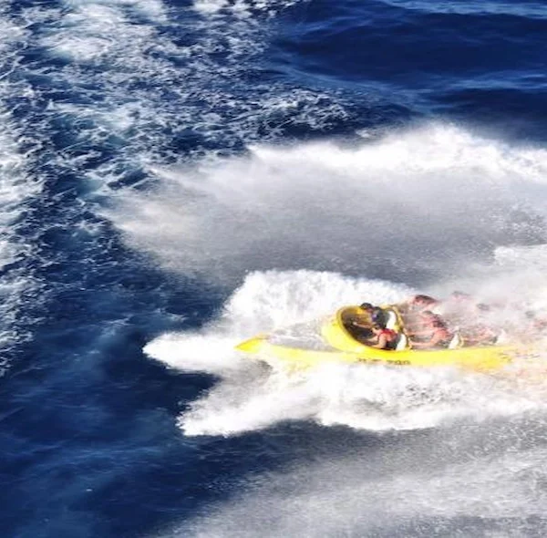 A high-angle overhead shot of a yellow speedboat carving through deep blue water, surrounded by large white wake and spray.