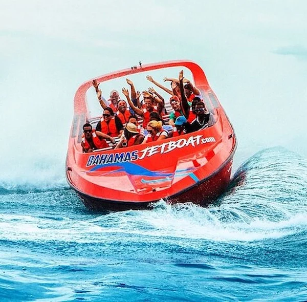 A red Bahamas Jet Boat filled with passengers in orange life vests performing a high-speed maneuver on the ocean.
