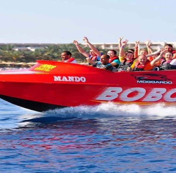 A bright red "Bobos" jet boat named "Mando" full of cheering tourists speeding across blue water near a tropical beach resort