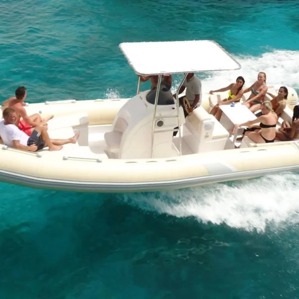 A white bullet rigid inflatable boat (RIB) with a T-top canopy carrying several passengers through turquoise tropical water.
