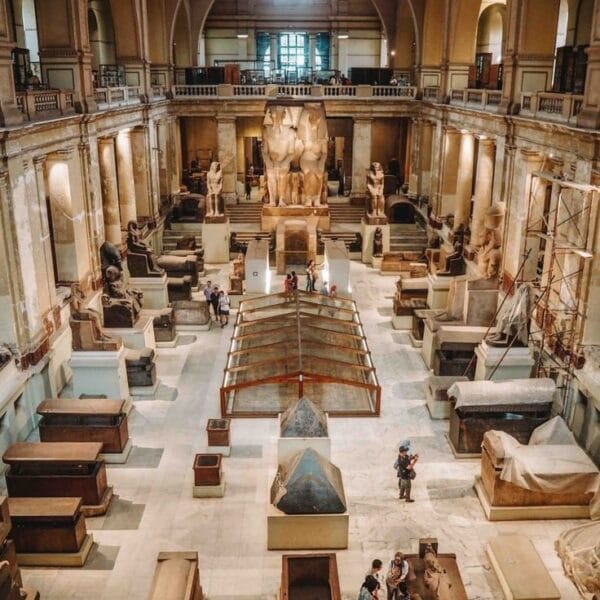 The vast interior hall of the Egyptian Museum in Cairo, filled with ancient stone sarcophagi, colossal statues, and historical artifacts