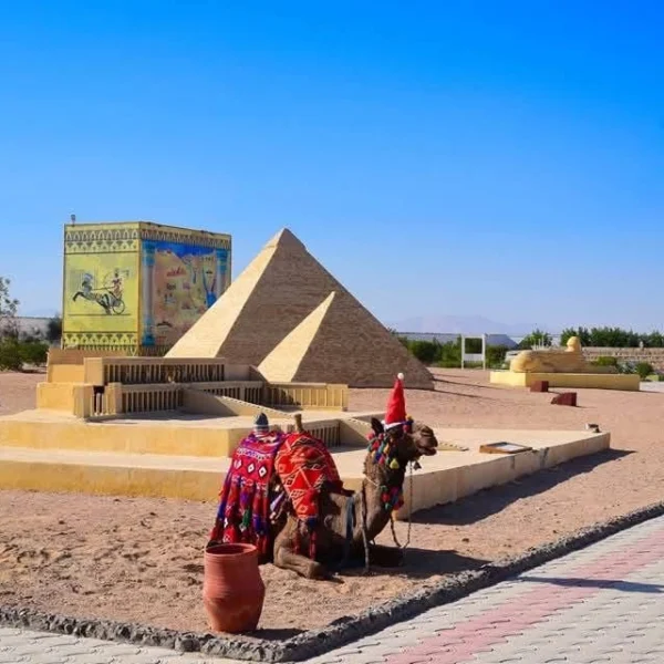 A miniature replica of the Temple of Hatshepsut and a pyramid with a real camel wearing a Santa hat in the foreground.