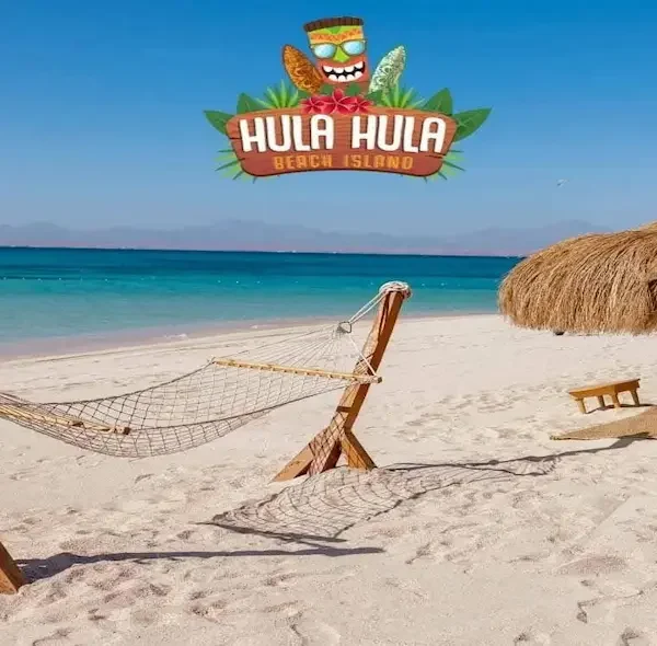A beach hammock on white sand at Hula Hula Island with a straw umbrella and the colorful Hula Hula Beach Island logo in the sky.