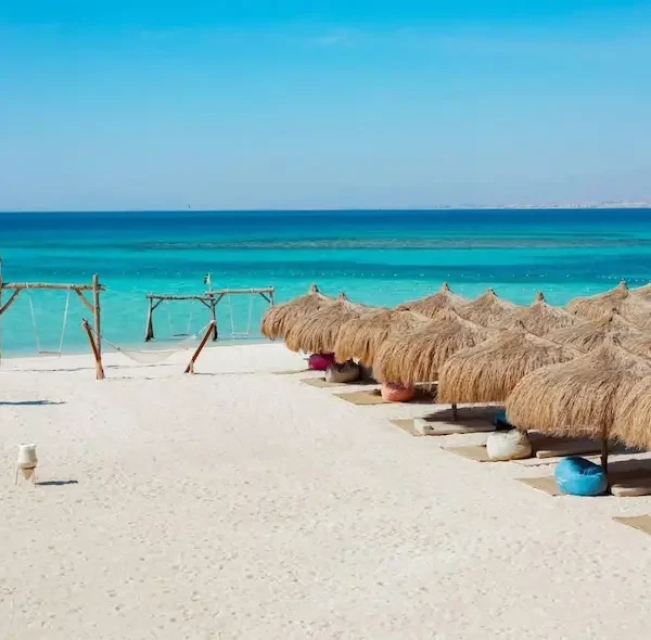 Turquoise sea view with snorkeling boats and straw umbrellas on the white sandy beach of Hula Hula Island in Hurghada.
