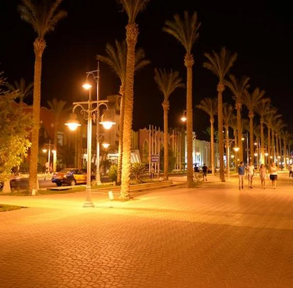 A brightly lit pedestrian promenade at night lined with tall palm trees and warm street lamps in Hurghada, Egypt