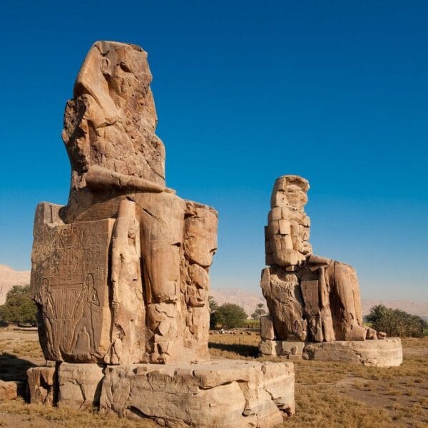 Luxor Over Day: The two massive stone statues of Pharaoh Amenhotep III, known as the Colossi of Memnon, standing in the Theban Necropolis