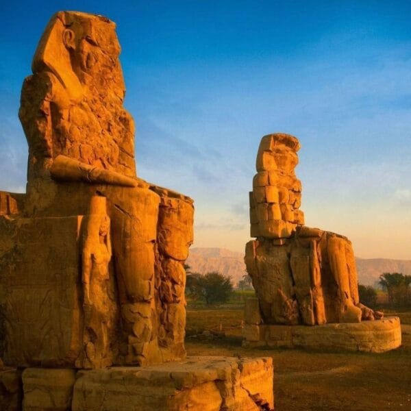 Luxor Over Day: The ancient Colossi of Memnon statues glowing in the golden light of sunset in Luxor