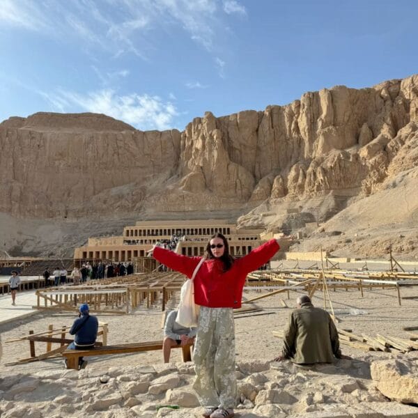 Luxor Over Day: A tourist posing with open arms in front of the historic Temple of Hatshepsut at Deir el-Bahari in Luxor