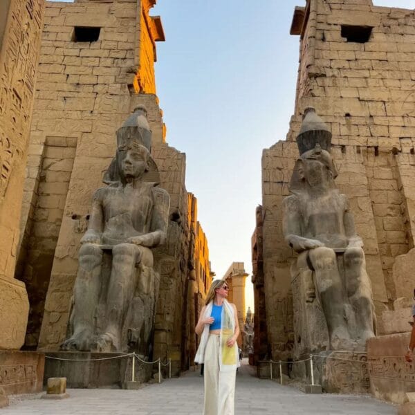 Luxor Over Day: A tourist walking toward the magnificent entrance of Luxor Temple, flanked by the colossal seated statues of Ramesses II and a towering obelisk