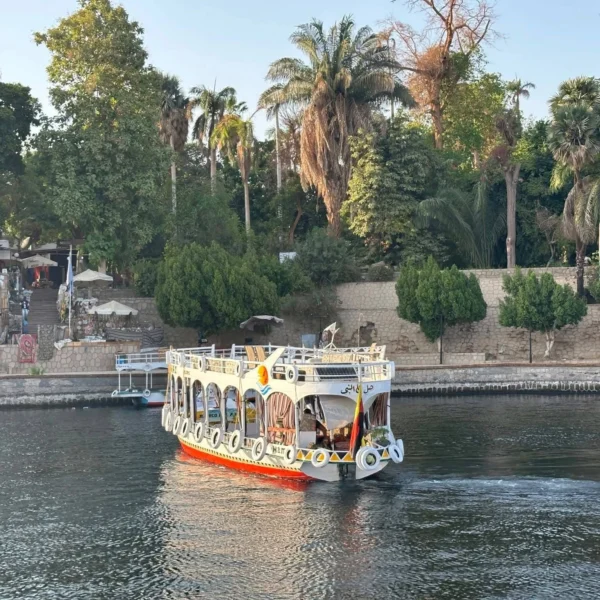 A small traditional Egyptian motorboat, often called a launch, docked on the banks of the Nile River in Luxor with the West Bank hills in the background.