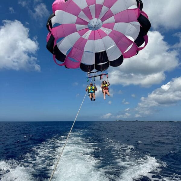 Parasailing Hurghada: Two tourists enjoying a parasailing experience under a pink, white, and black parachute with a clear blue sky and ocean view