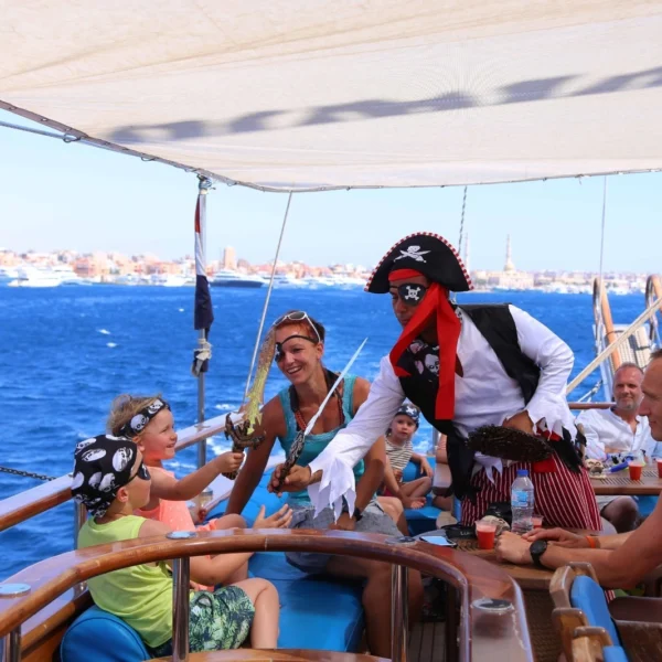A crew member dressed as a pirate interacts with the children and joins them in playing with plastic swords on the deck