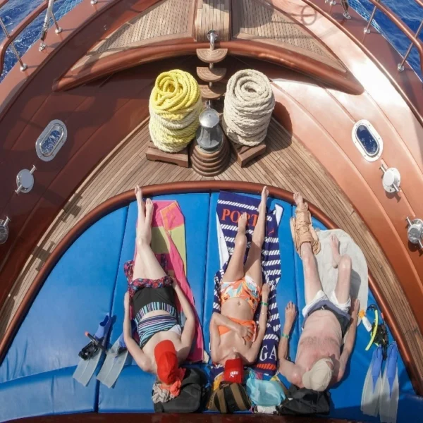 Tourists lie on blue mattresses at the front of the luxurious wooden ship to enjoy sunbathing under the clear sky