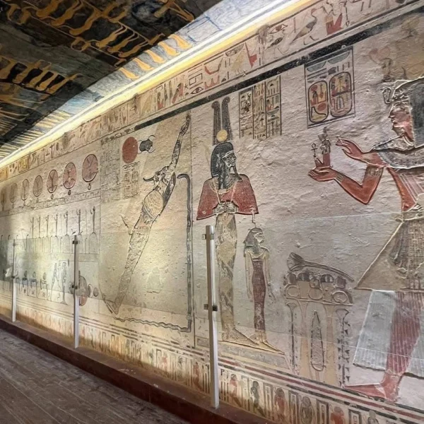 A vibrant ancient Egyptian wall painting in tomb KV9 showing the solar barque of Ra and celestial figures on a golden-yellow background.