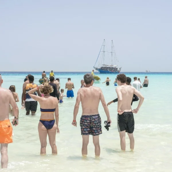 A group of tourists enjoy the shallow turquoise waters near a sandy beach