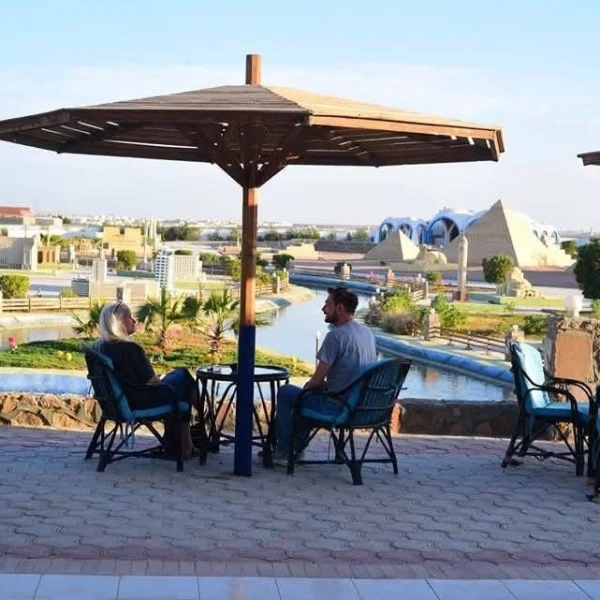 Two people sitting under a wooden umbrella at a terrace overlooking the miniature landmarks.