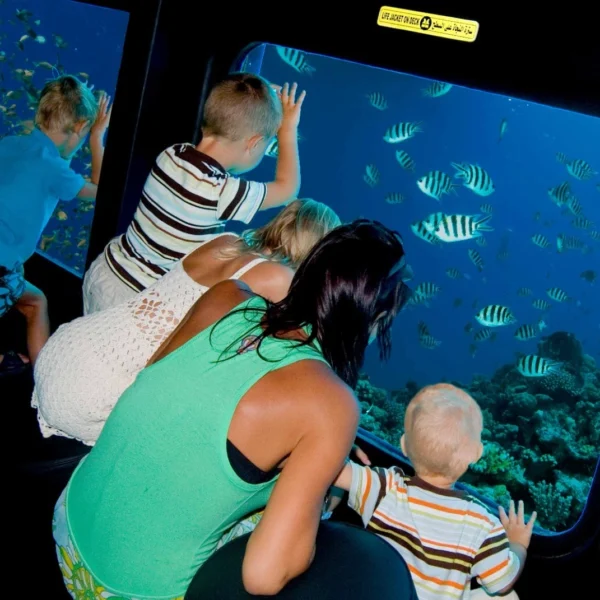 A family with children watching schools of striped fish and coral reefs through the large glass windows of an underwater submarine